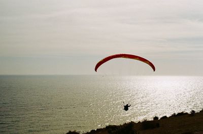 Silhouette person paragliding over sea against sky