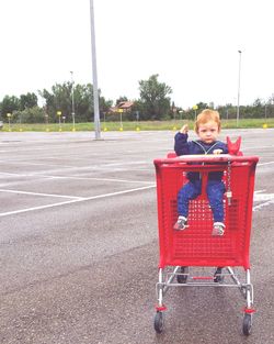 Portrait of boy sitting on shopping cart against sky