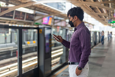 Young asian man using smartphone while waiting for subway or sky train.