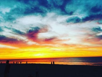 Silhouette people on beach against dramatic sky during sunset