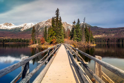 Footbridge over lake with mountains in background against cloudy sky