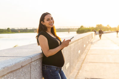 Portrait of smiling young woman standing on mobile phone against sky