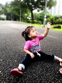 Full length of cute baby girl sitting on road against trees