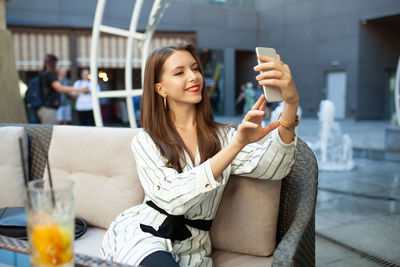 Young woman using mobile phone while sitting in laptop