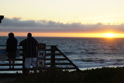 Rear view of people looking at sea against sky during sunset