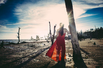 Rear view of woman standing by tree at beach on sunny day