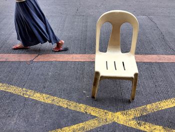 Low section of woman walking by chair on road