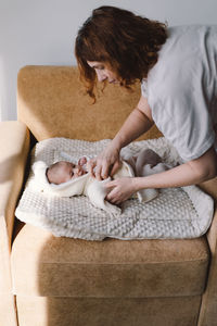 Mom dresses cute newborn little baby boy in a jumpsuit.