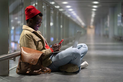 Side view of man using smart hone while sitting at footbridge