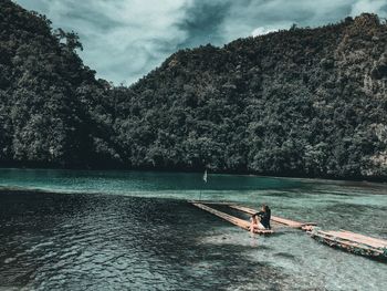 Woman sitting on wooden raft in river against sky