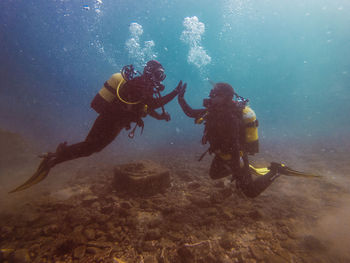 Side view unrecognizable divers giving high five together on the bottom of the ocean during scuba diving
