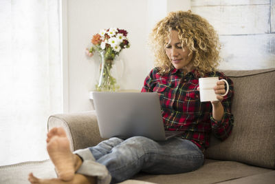 Full length of woman using laptop while sitting on sofa at home