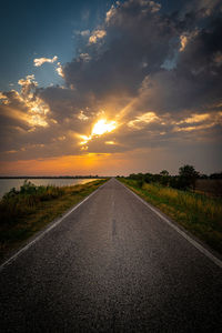 Road amidst field against sky during sunset