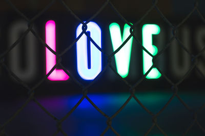 Close-up of illuminated text on chainlink fence