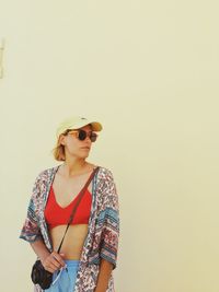 Portrait of young woman wearing sunglasses while standing against white background