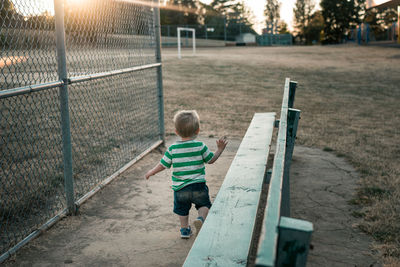 Rear view of cute boy walking on playing field during sunset