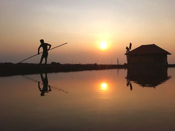 Silhouette man by lake against sky during sunset