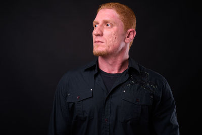 Portrait of young man standing against black background