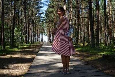 Full length of woman wearing red dress standing on footpath amidst trees at forest