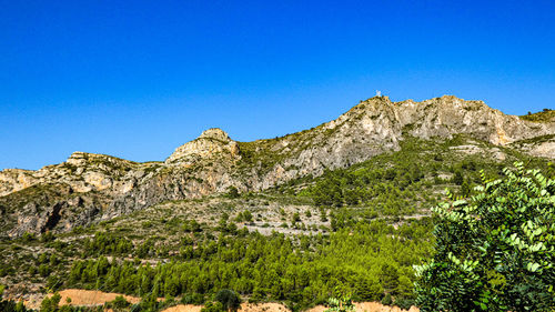 Low angle view of rocky mountains against clear blue sky