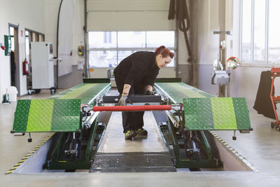 Female mechanic using hydraulic lift in auto repair shop