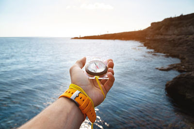 A man's hand with a wristwatch bracelet holds a magnetic compass against the background 