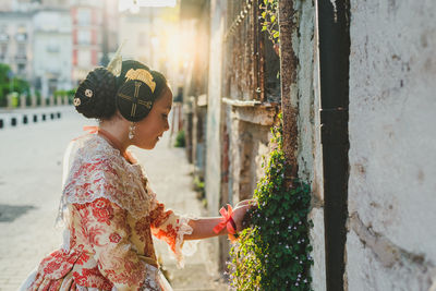 Side view of girl touching plants against wall