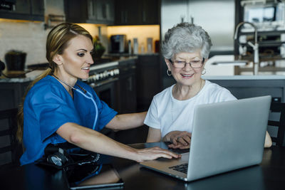 Home caregiver and senior woman looking at laptop computer on dining table