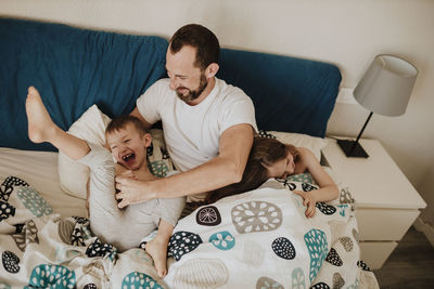 Father playing with cheerful children on bed at home
