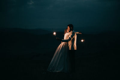 Woman standing against illuminated lighting equipment at night