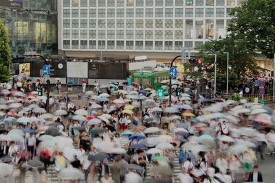 Blurred image of people walking with umbrella on road in city during rainy season