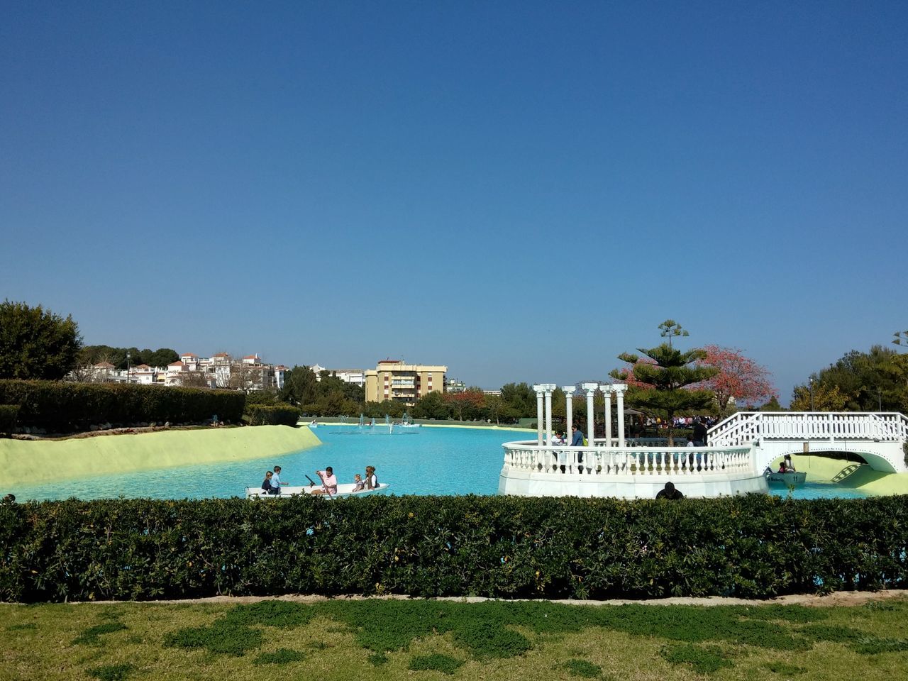 clear sky, copy space, blue, water, lifestyles, leisure activity, person, men, tree, relaxation, grass, built structure, building exterior, architecture, sitting, large group of people, day, sunlight, vacations