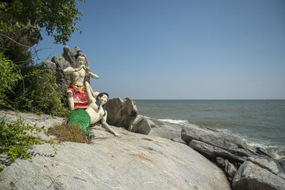 Rear view of woman standing on rock by sea against sky