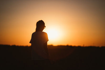 Woman standing on field against sky during sunset