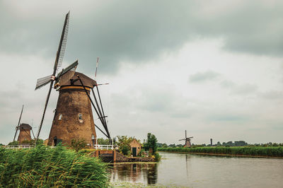 Traditional windmill by lake against sky