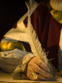 Midsection of person wearing traditional clothing writing with feather in paper