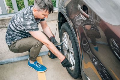 A man pumps the wheel of a car with a pump at car parking