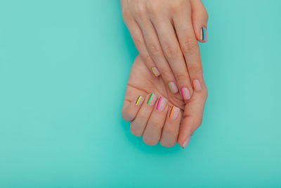 Close-up of woman with colorful fingernails on blue background