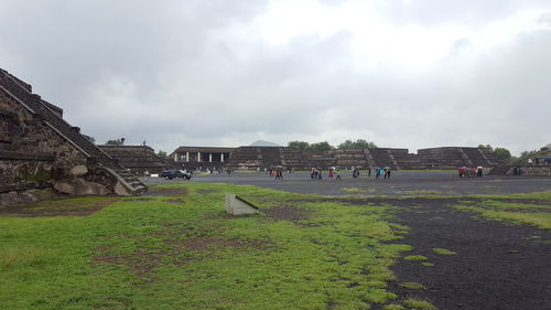 People on grassy field against cloudy sky