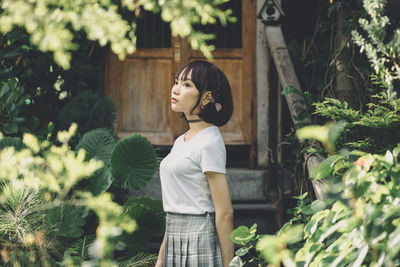 Young woman looking away while standing against plants