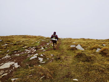 Full length rear view of backpacker walking on mountain against clear sky