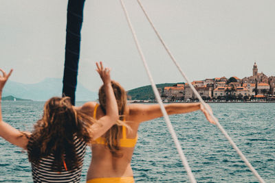 Women enjoying while standing on boat in sea against sky