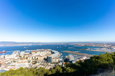 High angle view of city by sea against clear blue sky