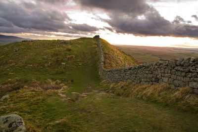 Hadrians wall on field against cloudy sky during sunset