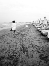 Rear view of woman walking at beach against sky