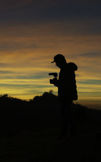 Silhouette man photographing against sky during sunset