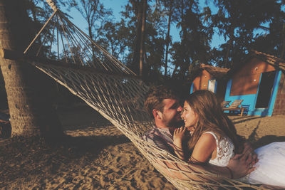 Young couple romancing while lying on hammock at beach during sunset