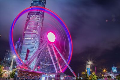 Illuminated ferris wheel in city against sky at night