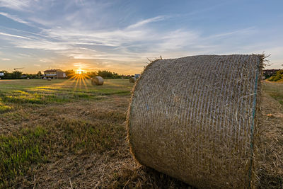 Hay bales on field against sky during sunset