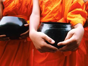 Midsection of monks holding container while standing in shrine